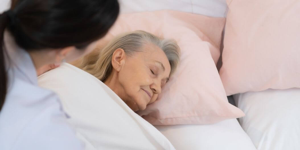 Female Nurse Checking on Sleeping Elderly Woman in Bed at an Assisted Living Facility