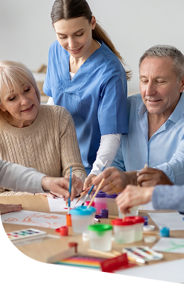 Female Nurse Assisting Elderly Woman and Man with Craft Activity in Independent Living Facility Female Nurse Assisting Elderly Woman and Man with Craft Activity in Independent Living Facility